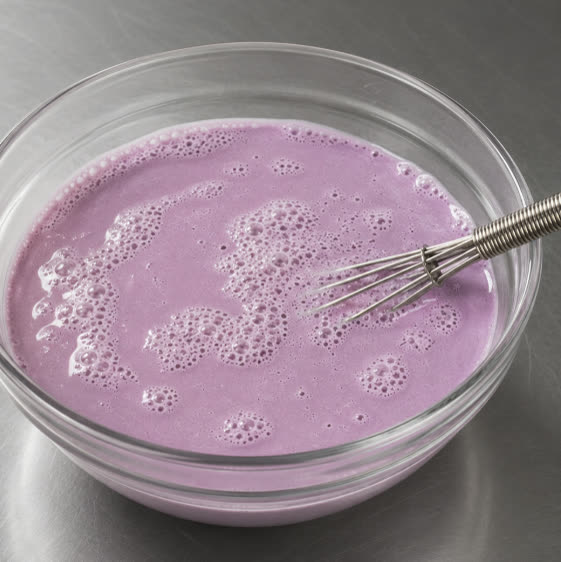 Mélange de laits à l'ube violet fouetté dans un bol en verre | Ube Nolia
