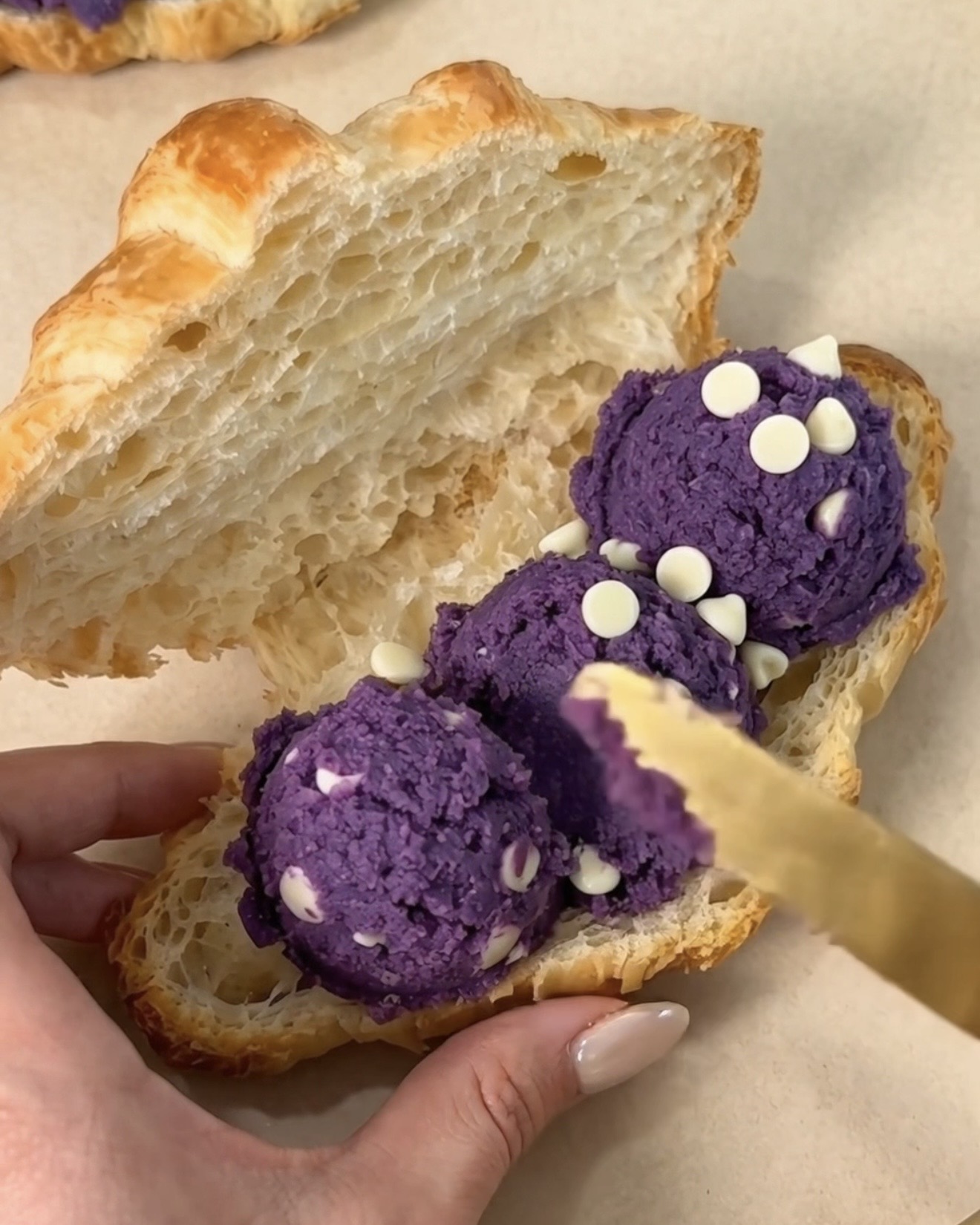 Étaler des boules de pâte à cookie chocolat blanc et ube (igname violette) UBE NOLIA® à l'intérieur d'un croissant artisanal pur beurre coupé pour faire un crookie à l'ube