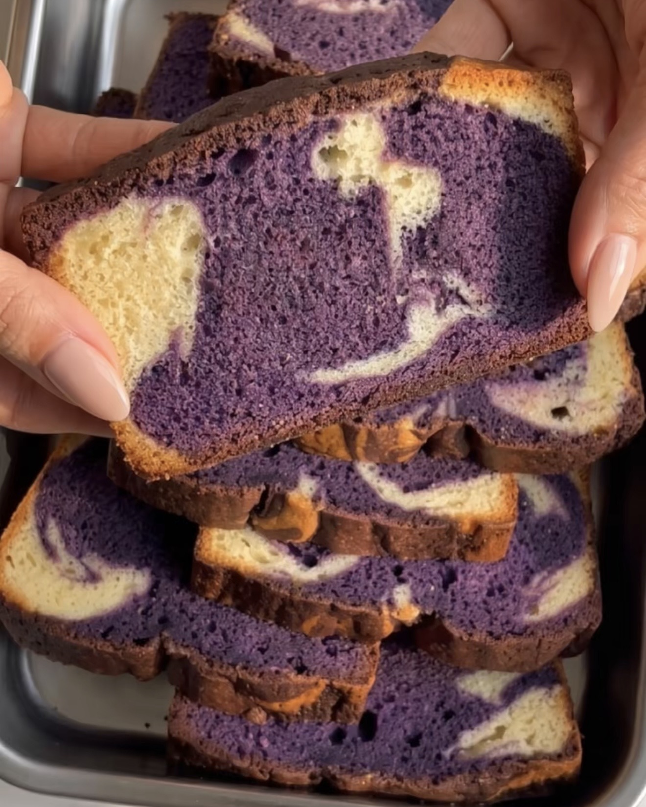 Main tenant une tranche de gâteau marbré ube avec un tourbillon violet et vanille, cuit avec la poudre d'ube UBE NOLIA