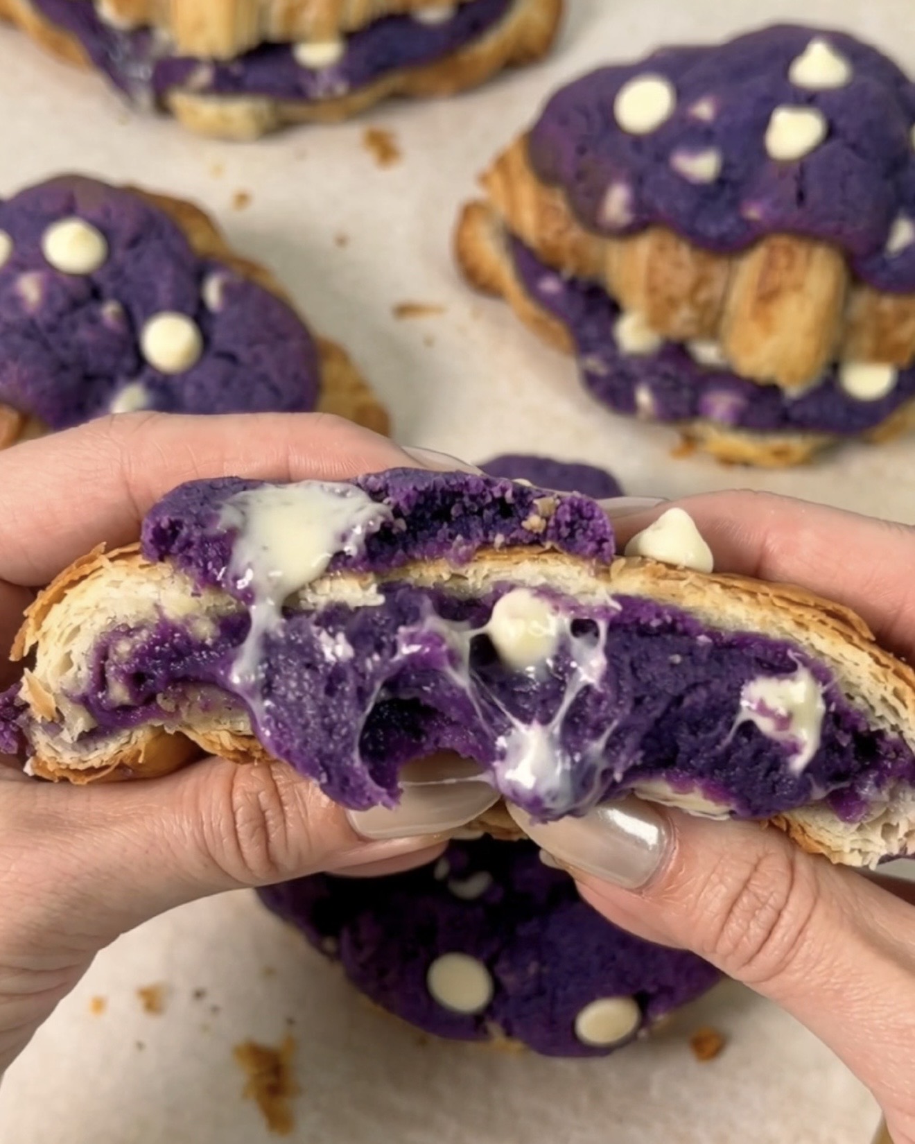 Crookies à l'ube UBE NOLIA® fraîchement cuits et ouverts pour révéler un centre de cookie chocolat blanc et ube (igname violette) violet fondant qui coule entre des couches de croissant dorées