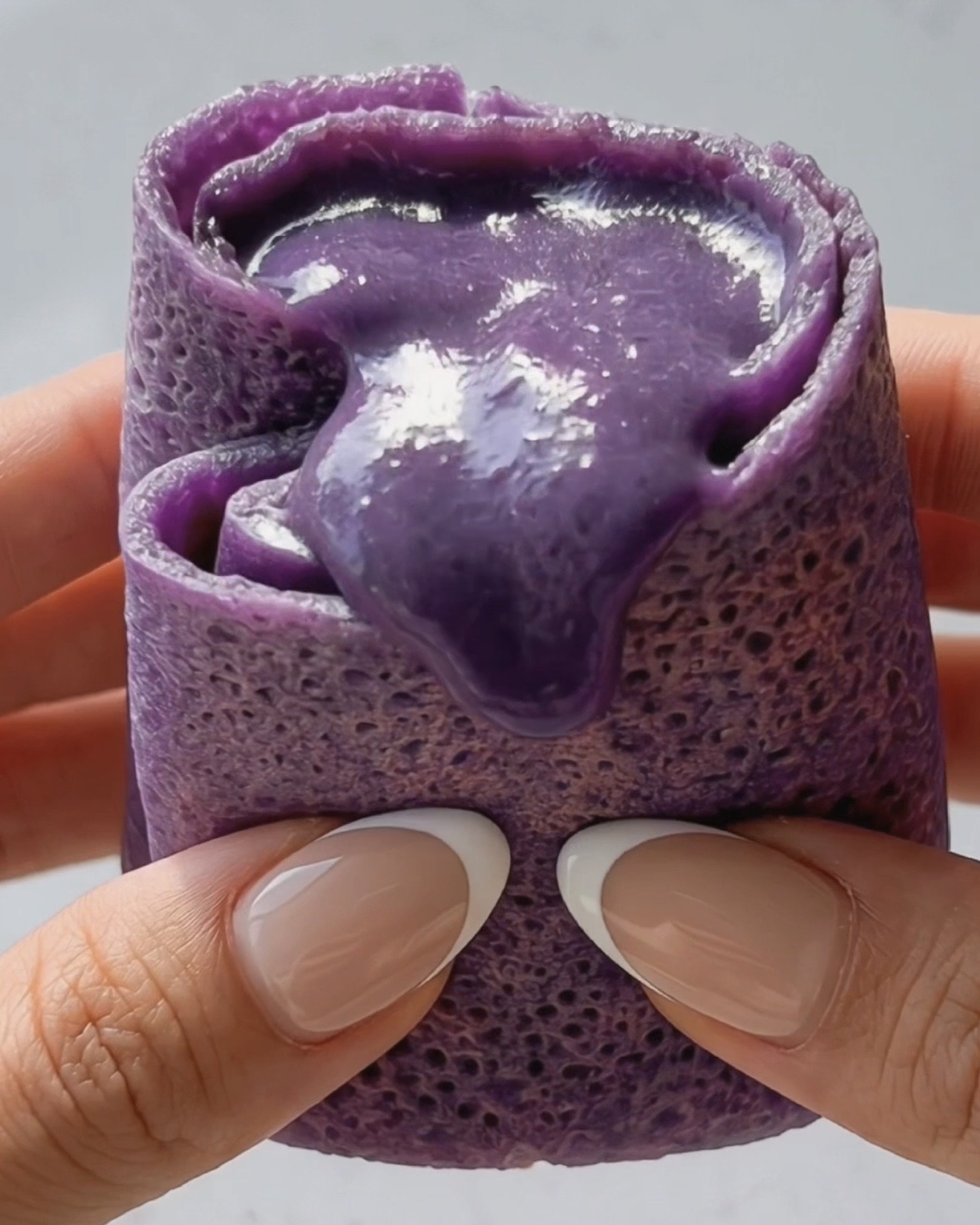 Crêpe ube dadar gulung coupée en deux montrant la garniture soyeuse et crémeuse d'ube halaya violette à l'intérieur