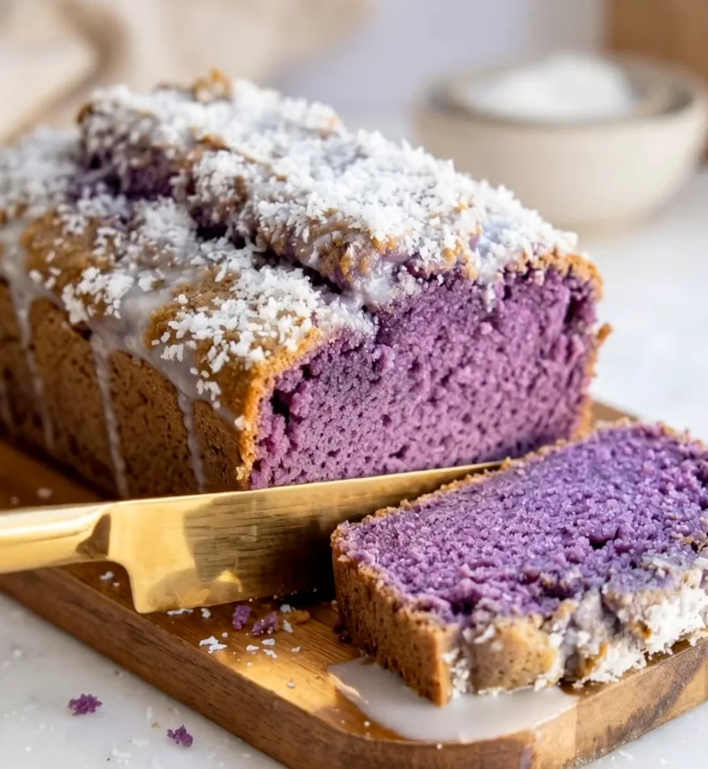 Cake loaf ube coco violet tranché sur une planche en bois avec garniture de coco blanche et un couteau doré, recette Ube Nolia