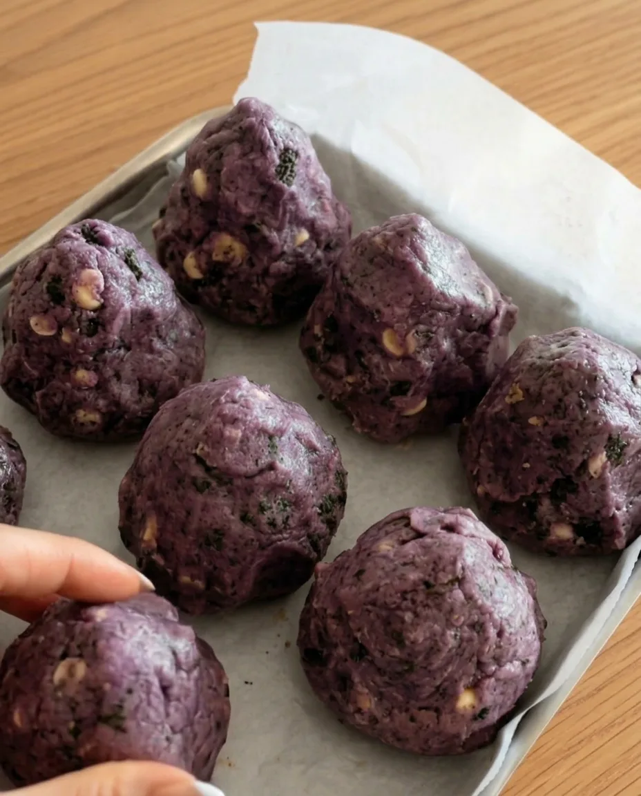 Boules de pâte à cookies Ube Oreo violettes sur papier sulfurisé prêtes à congeler pour des cookies épais style New York
