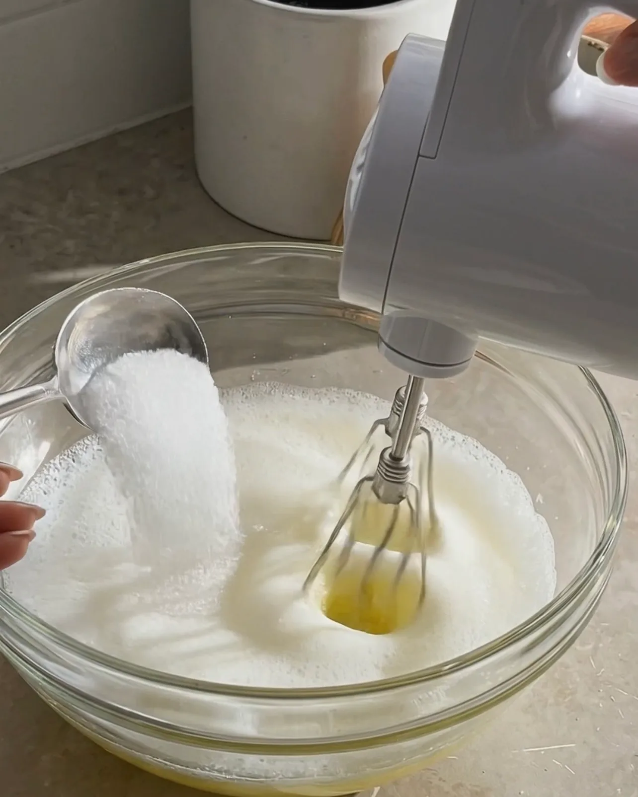 Ajout de sucre à des blancs d'œufs mousseux en fouettant avec un batteur électrique pour le roulé à l'ube par Ube Nolia
