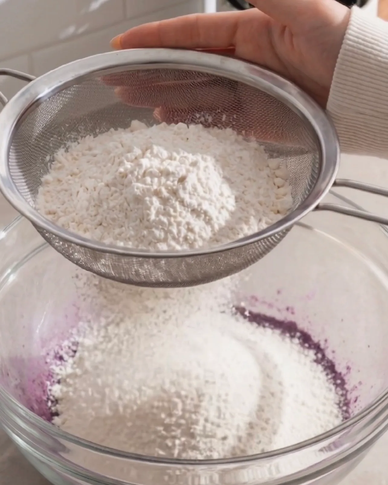 Tamisage de la farine à gâteau dans la pâte violette d'ube à travers une passoire fine par Ube Nolia