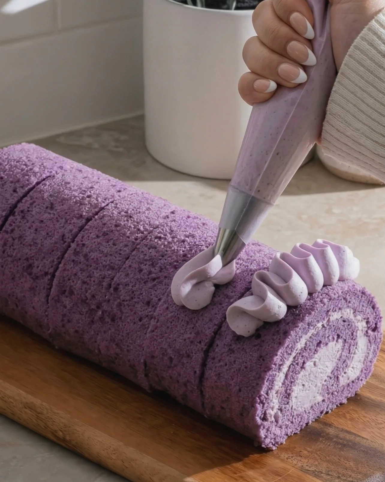 Pocher des rosettes décoratives de crème fouettée à l'ube sur le dessus du roulé à l'ube violet fini par Ube Nolia