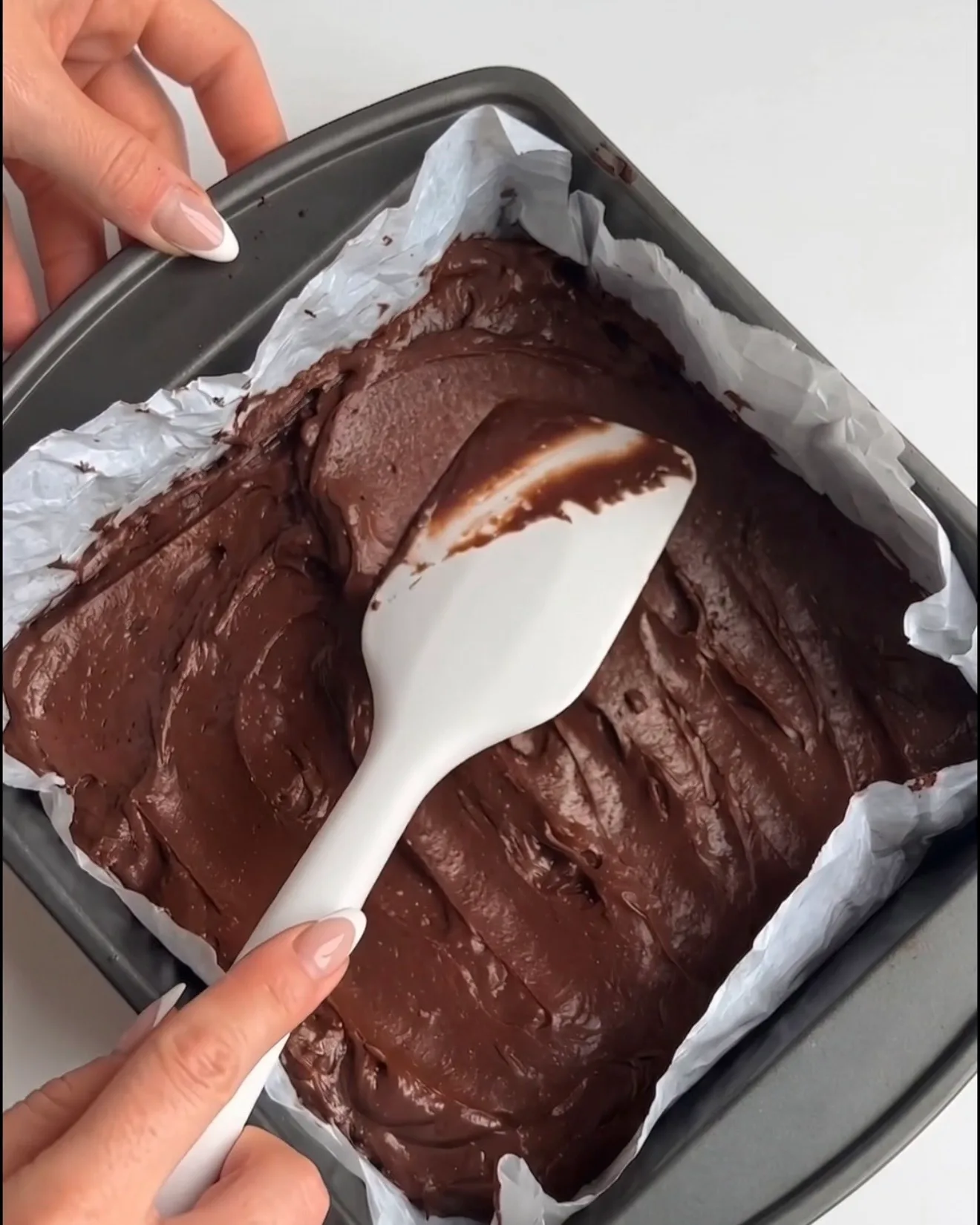 Pâte à brownie au chocolat Ube Dubai lisse étalée dans un moule carré tapissé de papier sulfurisé, prête à être cuite pour la recette Ube Nolia